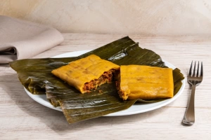 deliciosa hallaca venezolanas partida en dos sobre un plato y hojas de plátano